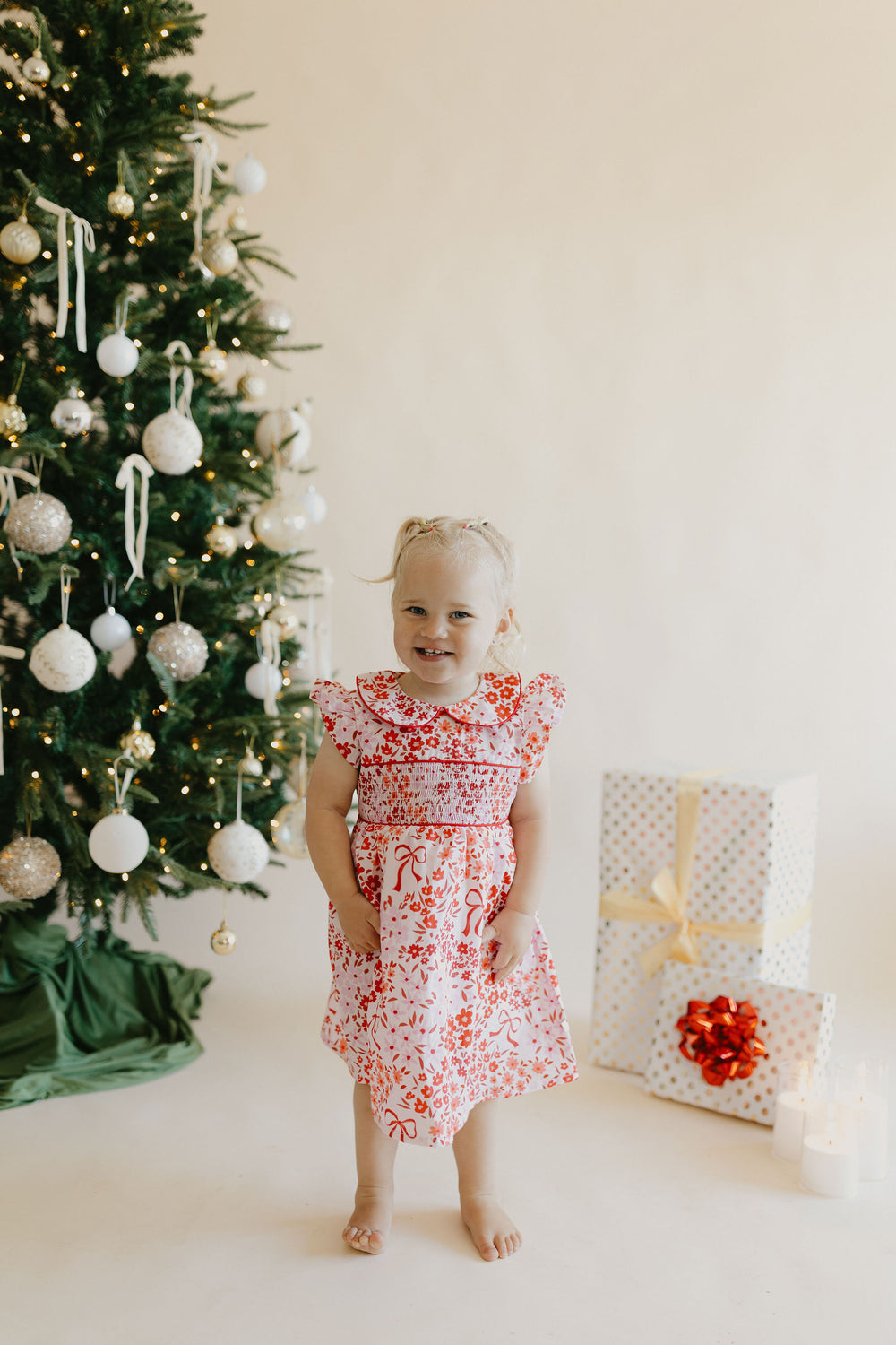 Little girl in a red floral Christmas dress beside a decorated Christmas tree
